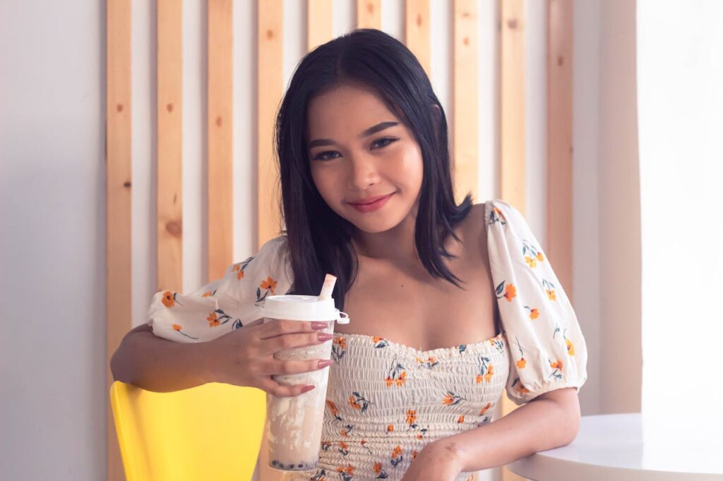 Smiling woman holding a cup of bubble tea, wearing a floral top indoors.