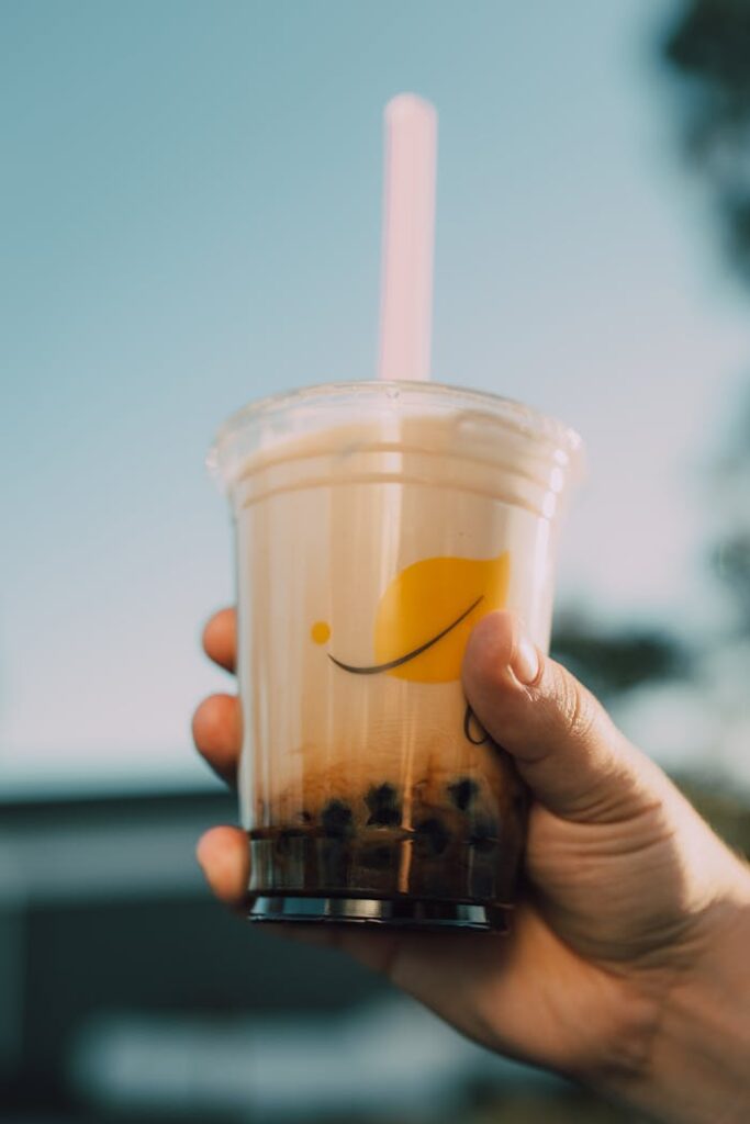 A hand holding a refreshing bubble milk tea with tapioca pearls against a sunny backdrop.
